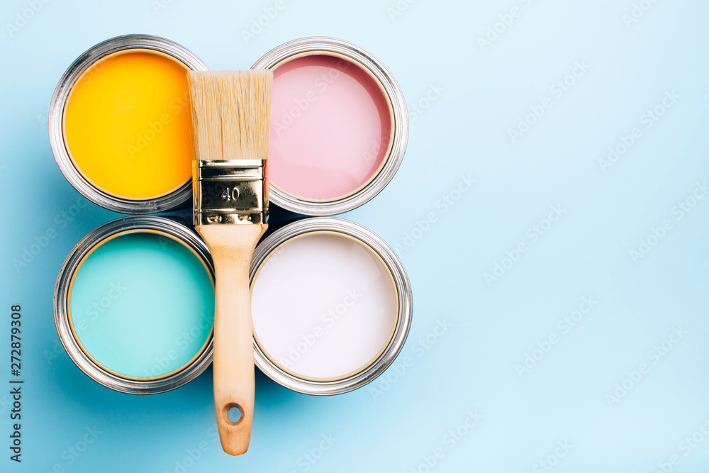 Brush with wooden handle on open cans on blue pastel background. Yellow, white, pink, turquoise colors. Renovation concept. Place for text. - obrazy, fototapety, plakaty 