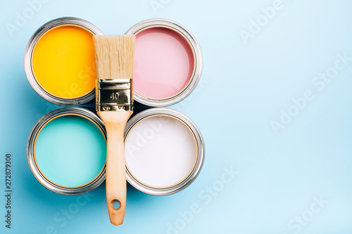Brush with wooden handle on open cans on blue pastel background. Yellow, white, pink, turquoise colors. Renovation concept. Place for text.