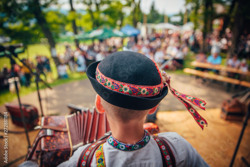 Young man playing on accordion in Slovak folk dress and folk hat. In front of the crowd photo