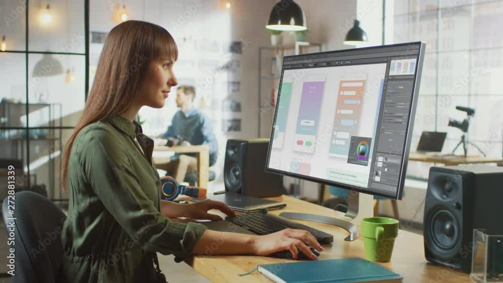 Beautiful Brunette Female Designer Works with Mobile App Interface on Her Personal Computer with Big Display. She Works in a Cool Office Loft. Beautiful Brunette Female Designer Works with Mobile App Interface on Her Personal Computer with Big Display. She Works in a Cool Office Loft.