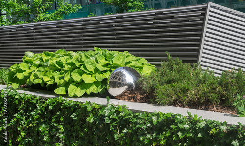 Reflective metal ball standing next to a bush, leafs and entrance to an underground parking lot