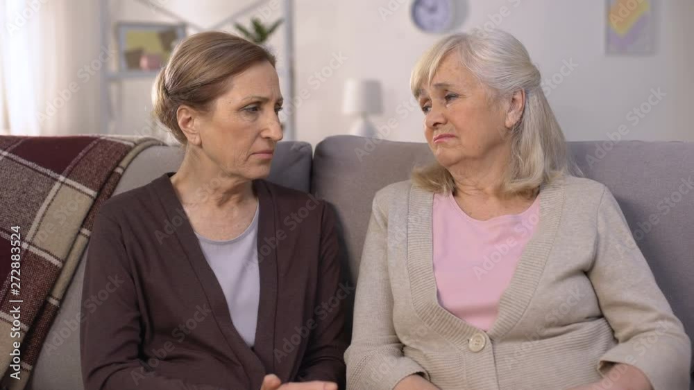 Mature friends supporting and comforting each other sitting on sofa pain of loss Mature friends supporting and comforting each other sitting on sofa pain of loss