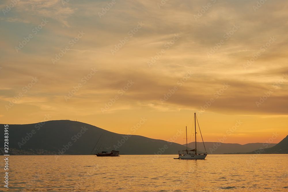 yacht with a small boat in the sunset light on the background of the mountains and the second frigate.