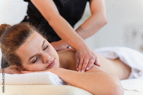Female massaeur hands doing massage to young woman in spa center.