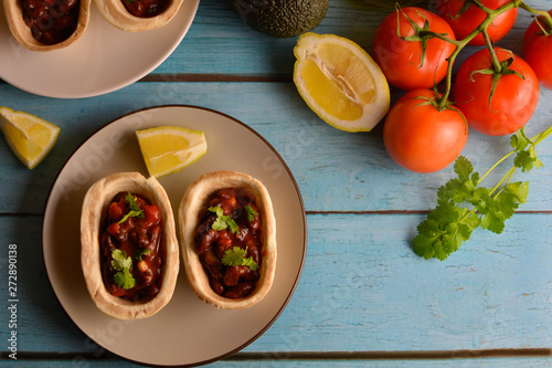 Traditional dish - Mexican tacos with ingredients beans and vegetables on the plate on a blue wooden background, top view. Lots of space for text and design.