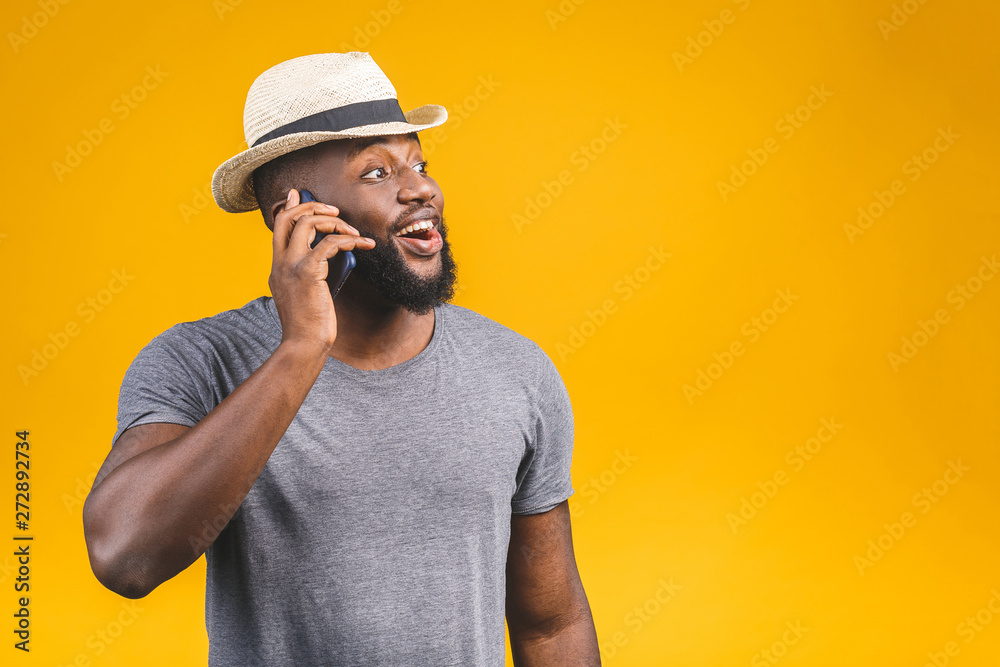 Portrait of a happy travel african american guy talking on mobile phone isolated against yellow background.