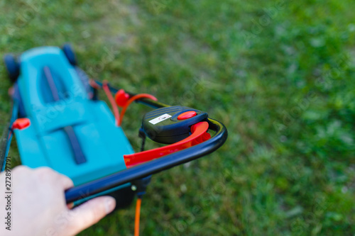 Man hand holding electric lawn mover machine to cutting short green grass.(Focus on the hands and handle of the lawn mower)