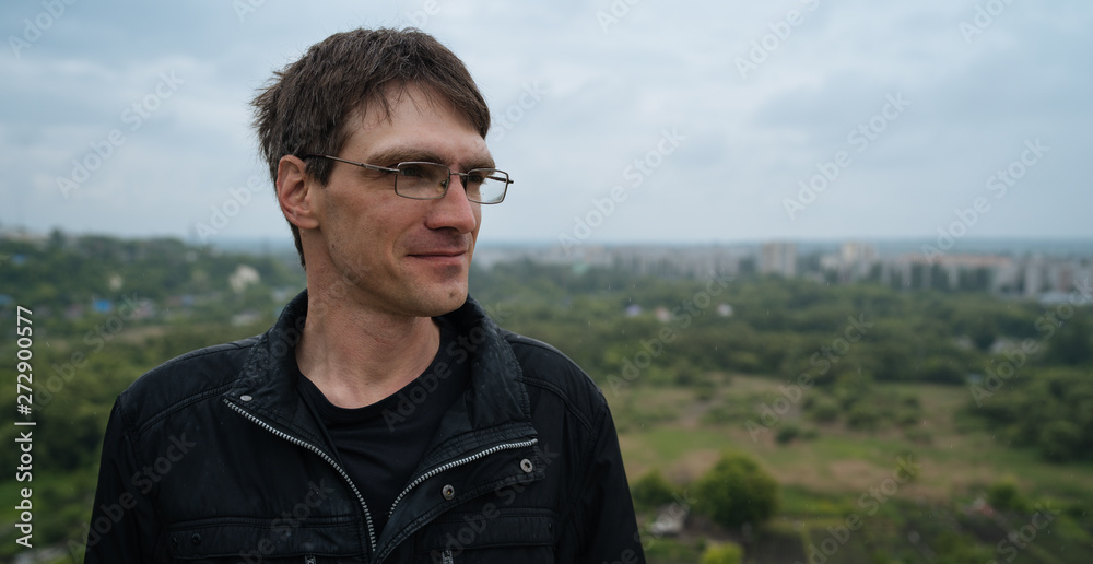 The man in glasses looks thoughtfully into the distance, standing on the street in the summer. Street style clothing The man in glasses looks thoughtfully into the distance, standing on the street in the summer. Street style clothing