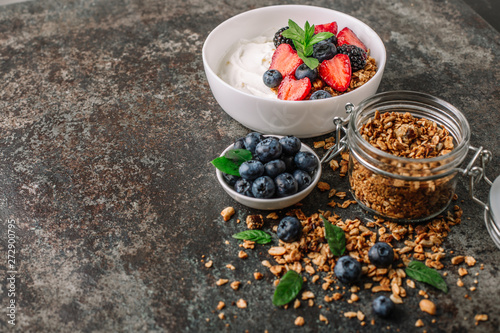 Healthy breakfast with granola, yogurt, fruits, berries on dark metal background. Summer homemade breakfast.