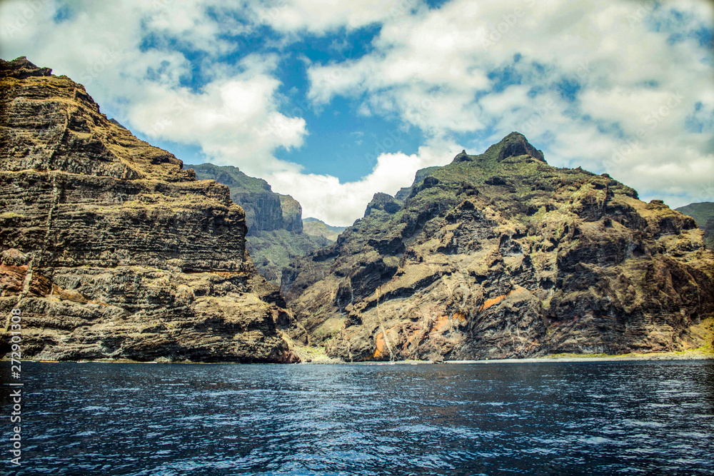 Steep high lava rock cliffs. Blue sea horizon, natural sky background.