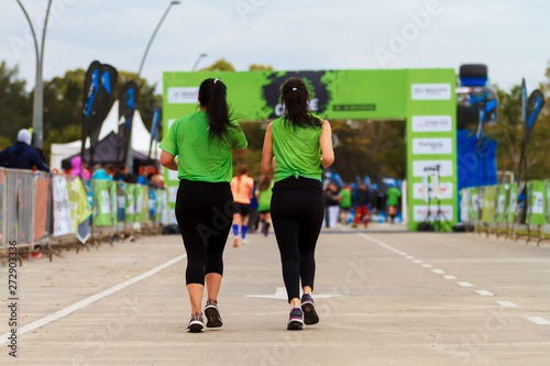 Two women seen from behind run towards the final line in a marathon