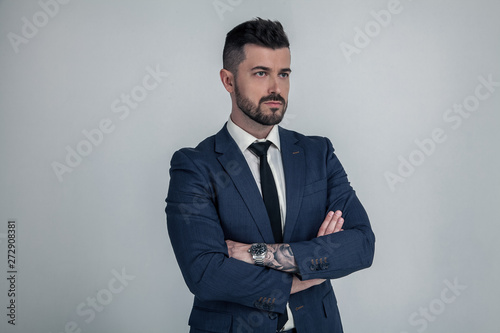 Portrait of handsome strict employer in blue suit standing in profile with crossed hands against gray background