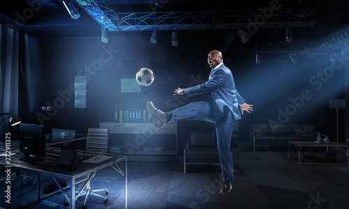 Black businessman in a suit playing footbal