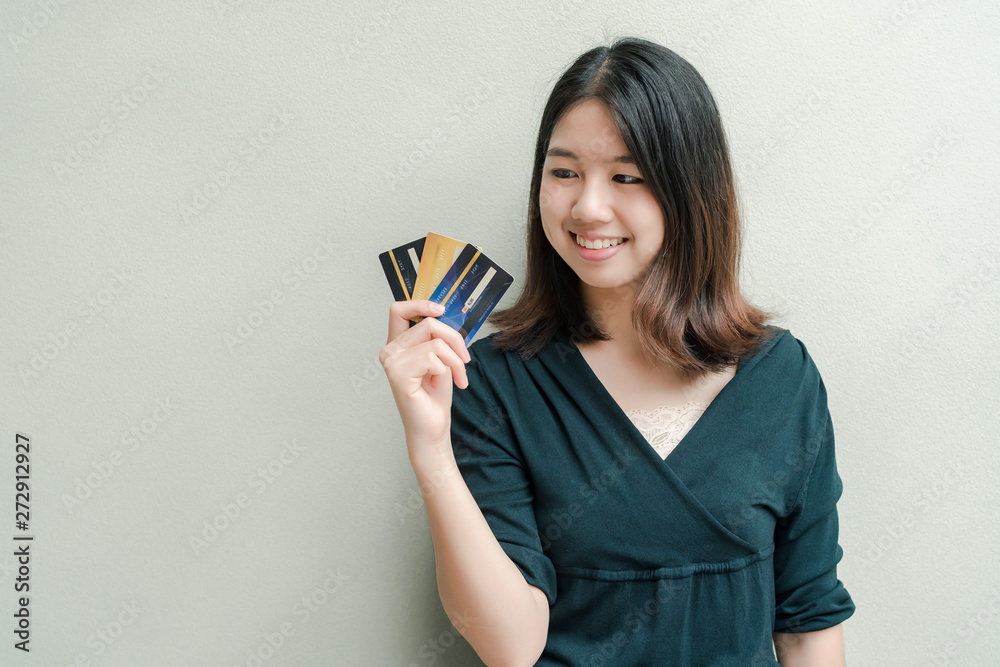 Asian beautiful woman Wearing a black shirt Have a credit card in hand Happy face Standing in the gray wall Asian beautiful woman Wearing a black shirt Have a credit card in hand Happy face Standing in the gray wall
