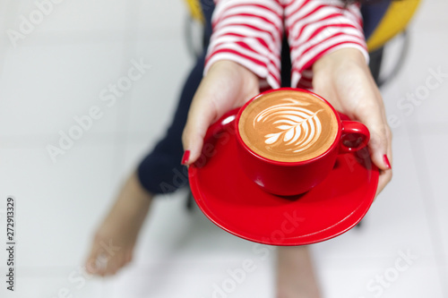 The woman's hand is holding a red cup of coffee latte art