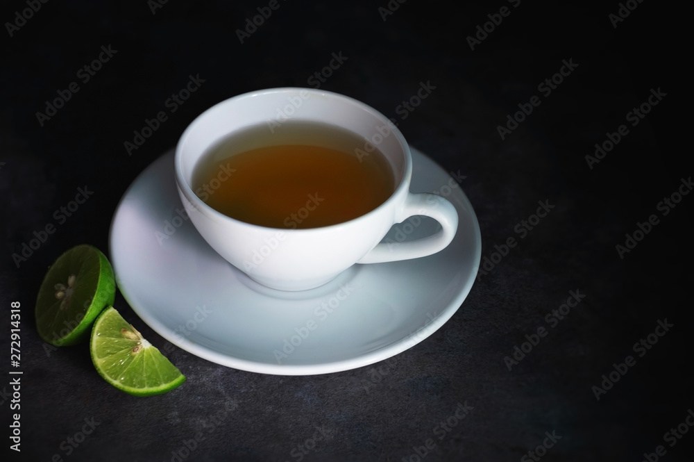 cup of tea on a rough black texture and crescent lime, dark background