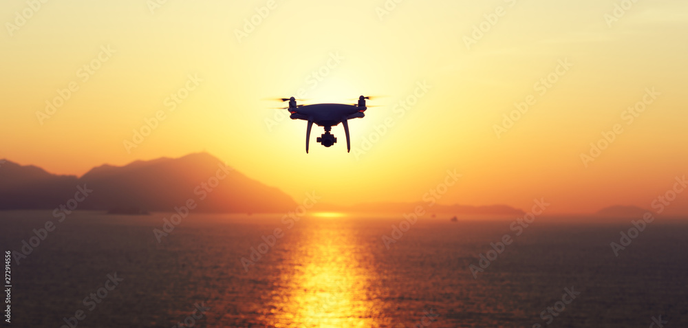 Silhouette of flying drone which taking photo over sunrise sea Silhouette of flying drone which taking photo over sunrise sea