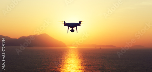 Silhouette of flying drone which taking photo over sunrise sea