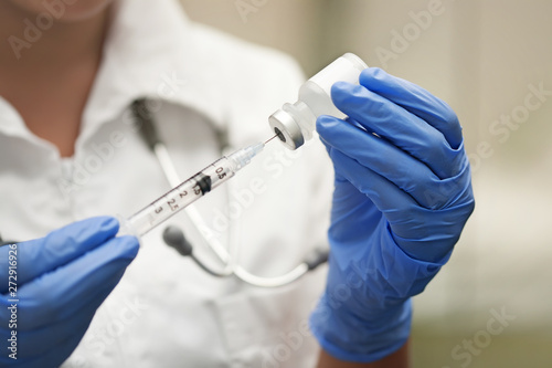 Medication nurse wearing protective gloves and white scrubs get a needle or shot ready for an injection. photo