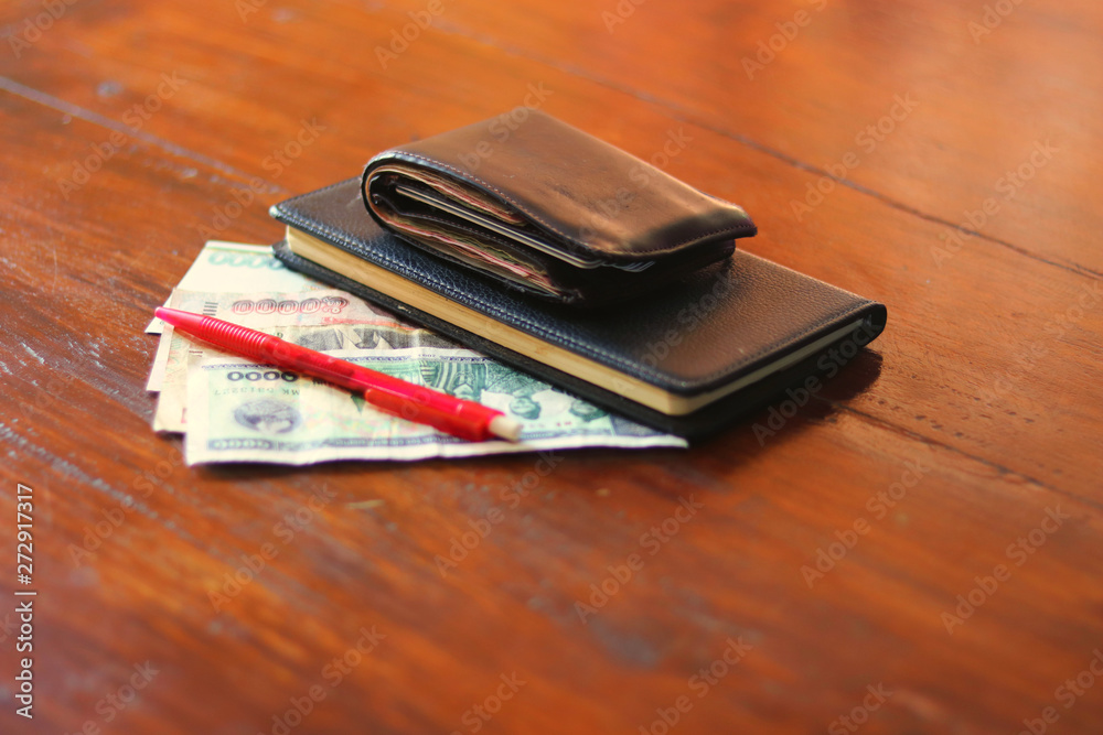Lao currency banknotes, pen and savings diary book laying on wooden table - Lao Kip banknotes for savings with a notebook for noting the savings as daily diary - money savings concept Lao currency banknotes, pen and savings diary book laying on wooden table - Lao Kip banknotes for savings with a notebook for noting the savings as daily diary - money savings concept