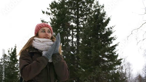 Handheld tracking with low angle of shivering young woman with backpack standing in forest on cold winter day and rubbing her hands to warm up