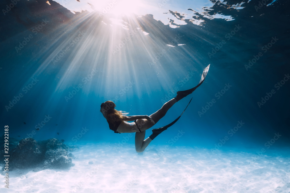 Young woman freediver glides over sandy sea with fins.