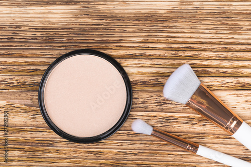 Foto powder to equalize the tone of the face and two brushes lie on a burnt wooden ba
