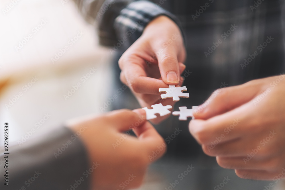 Closeup image of many people hands holding and putting a piece of white jigsaw puzzle together Closeup image of many people hands holding and putting a piece of white jigsaw puzzle together