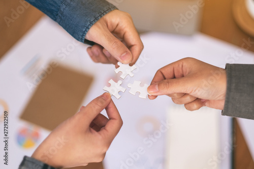 Closeup image of many people hands holding and putting a piece of white jigsaw puzzle together
