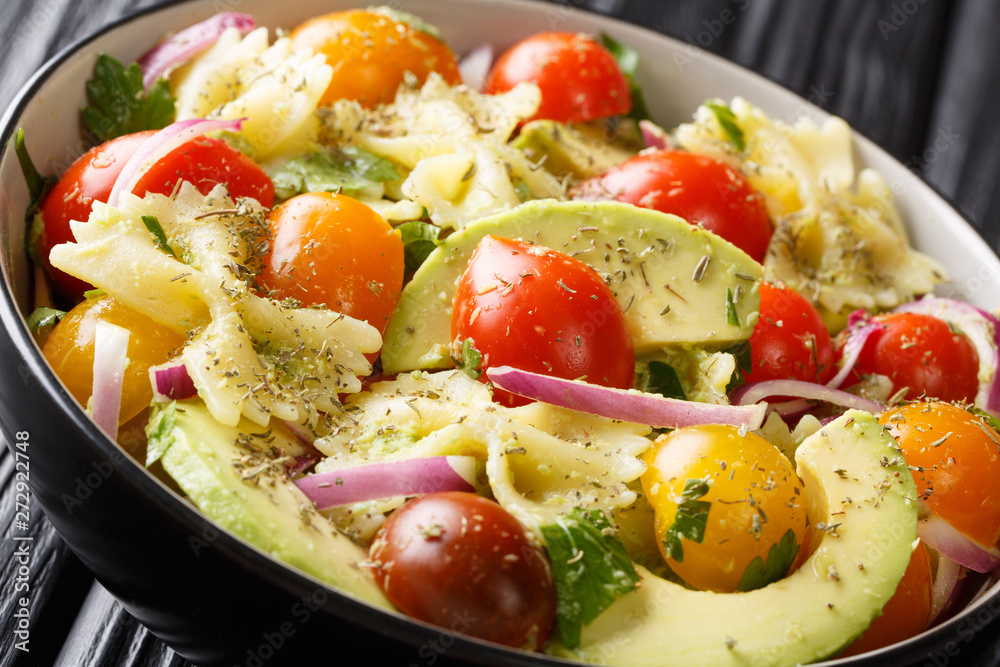 Italian pasta salad farfalle with ripe avocado, onions and tomatoes closeup in a bowl. horizontal