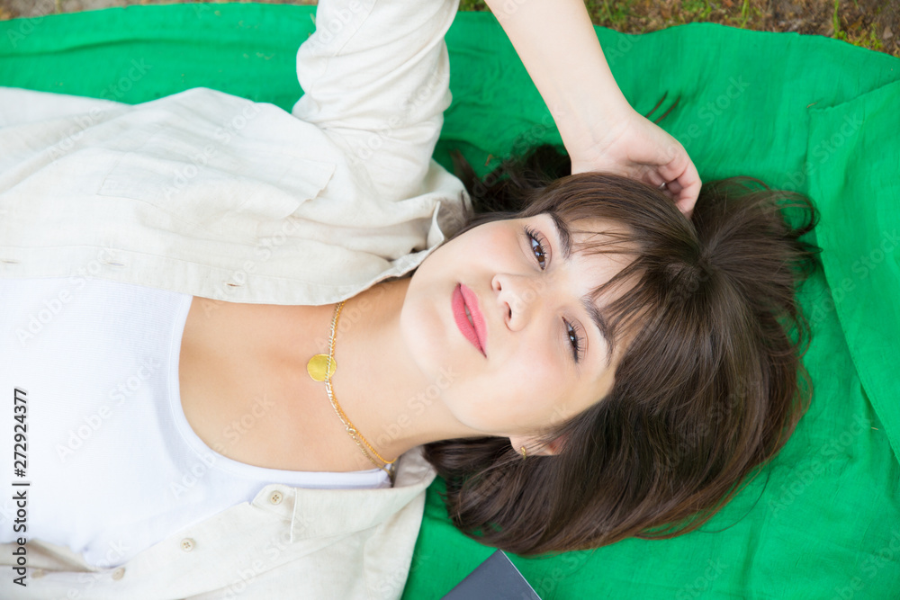 Closeup of happy serene girl relaxing outdoors. Top view of young woman lying on grass and smiling at camera. Leisure time outdoors concept Closeup of happy serene girl relaxing outdoors. Top view of young woman lying on grass and smiling at camera. Leisure time outdoors concept