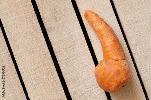 Strange funny homegrown carrot on wooden box background. Ugly food, unusual deformed fruits and vegetables, misshapen produce, food waste problem concept. Top view, copy space.