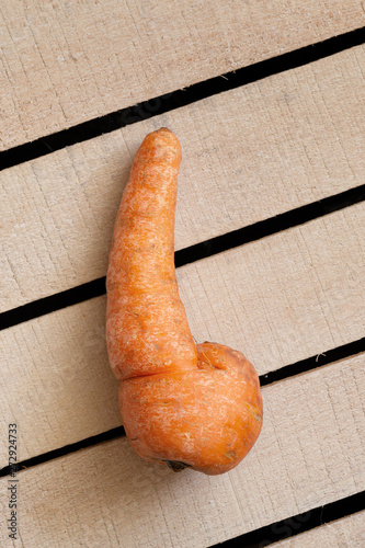 Trendy ugly organic carrot on wooden box background. Ugly food, unusual deformed fruits and vegetables, misshapen produce, zero waste concept. Top view, copy space, vertical