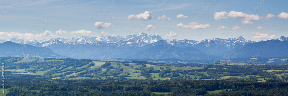 PEISSENBERG, BAVARIA / GERMANY - June 1, 2019: Huge panorama view of the Wetterstein Mountain Range (part of the alps). Blue sky and white clouds. Bavarian forests in the foreground.