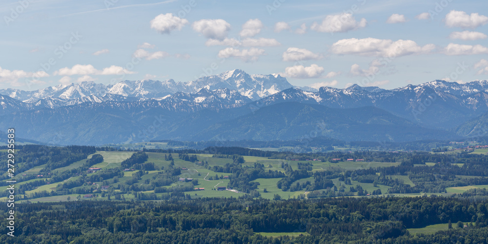 Distant view on the Wetterstein mountain range. In the middle Zugspitze mountain. Forests of the alpine foreland in the front. Fleecy clouds in the sky.