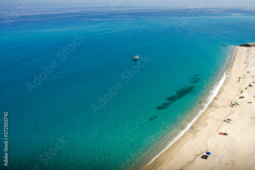 Turquoise water with boat and a line of sandy beach, background wallpapers. © vlamus