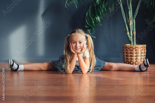 Nine year old girl with hair gathered in tails, white t-shirt, white socks and gray skirt laying on the floor with her head resting on hands.