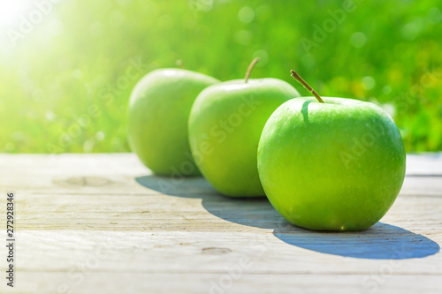 Freshly cropped geen apples on wooden table over grenn grass background.