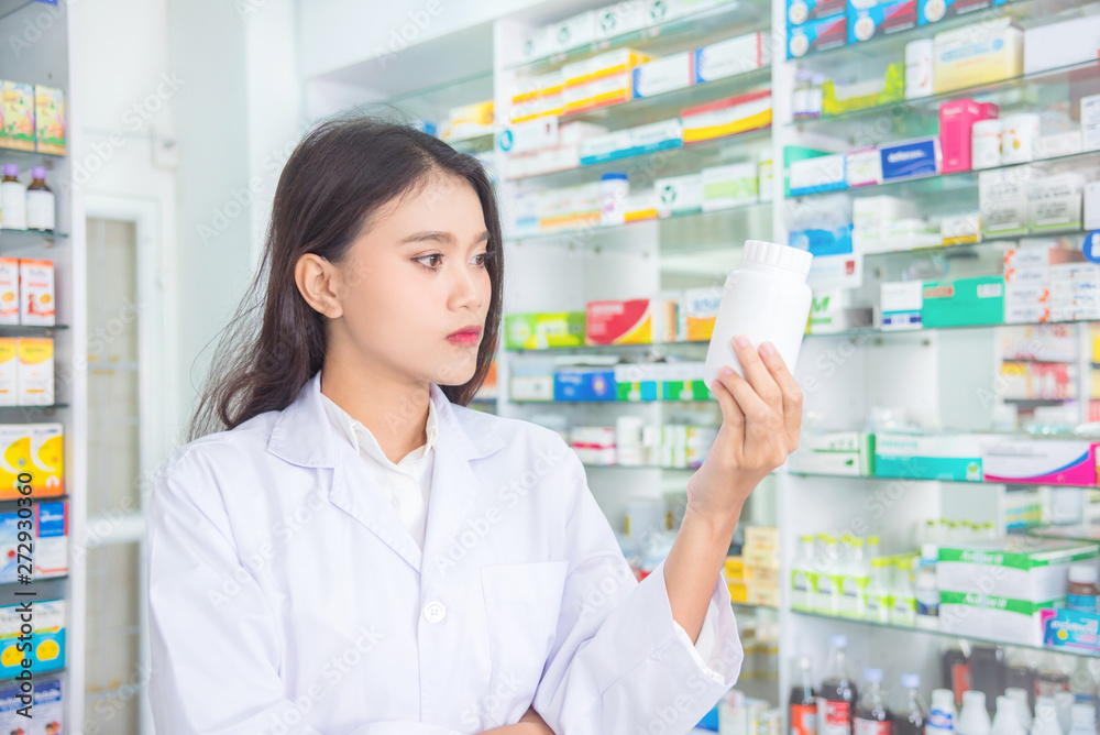 Beautiful asian pharmacist holding and looking at the medicine bottle in drugstore