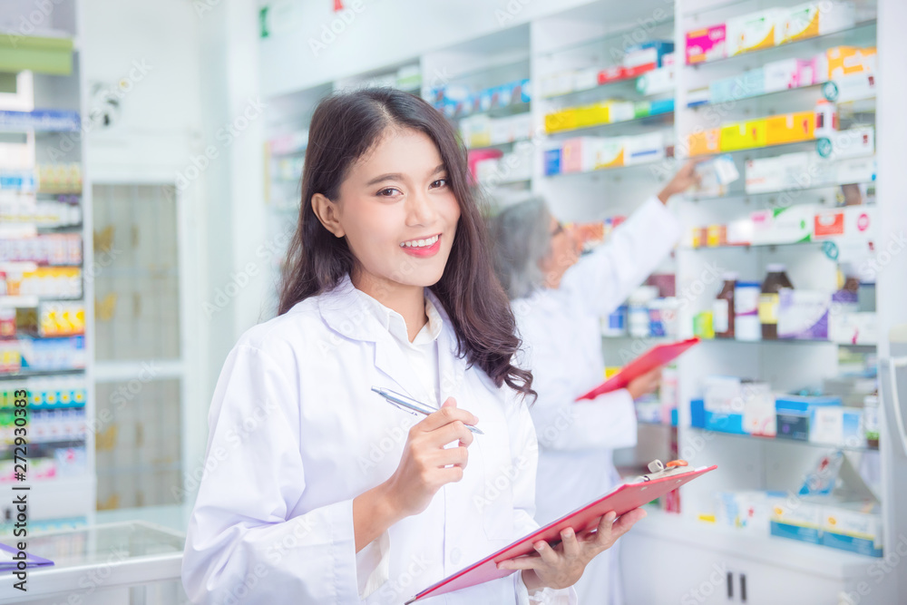 Beautiful asian pharmacist holding chart and smiles in drugstore