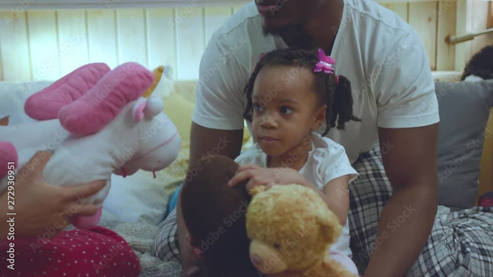 Portrait of sweet tender girl with braids sitting on fathers lap playing with favorite toys. Cheerful african family lying on comfort bed at home. family entertainment concept. Portrait of sweet tender girl with braids sitting on fathers lap playing with favorite toys. Cheerful african family lying on comfort bed at home. family entertainment concept.