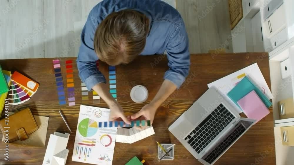 Top view shot with timelapse of creative male designer looking at house model and choosing color swatches, then typing on laptop Top view shot with timelapse of creative male designer looking at house model and choosing color swatches, then typing on laptop