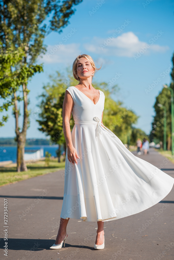 Elegant blonde hair woman in white midi dress at shore. Concept oа white code, fashionable lady, pretty dress and clothes Elegant blonde hair woman in white midi dress at shore. Concept oа white code, fashionable lady, pretty dress and clothes