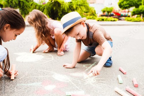 Small children draw in chalk among the city street.