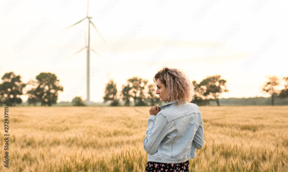young tanned curly haired woman in denim jacket and dress on the field of ripened wheat, sunset time young tanned curly haired woman in denim jacket and dress on the field of ripened wheat, sunset time