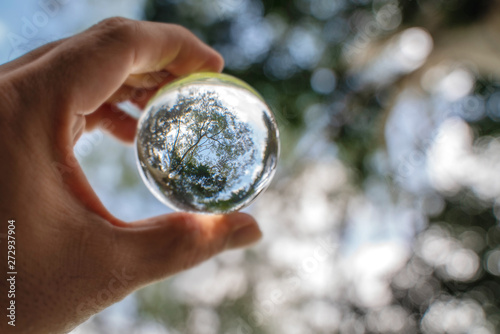 Reflection of blue sky, white clouds and trees in a glass ball in holding hand
