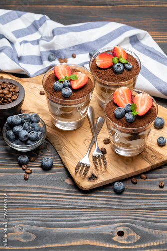 Classic tiramisu dessert with blueberries and strawberries in a glass on wooden background