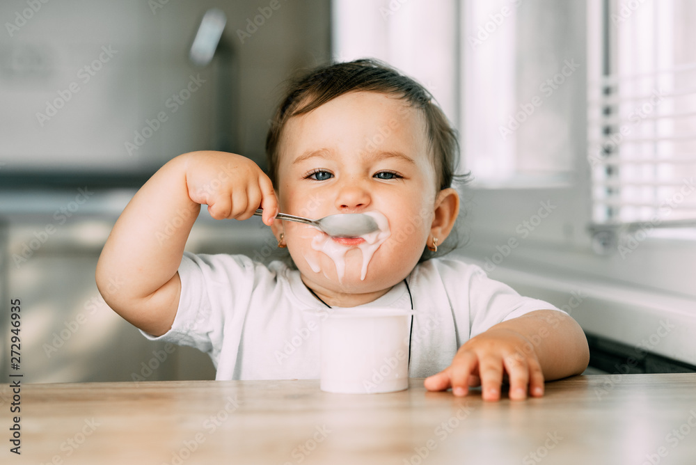 A little charming girl eats yogurt all smeared herself