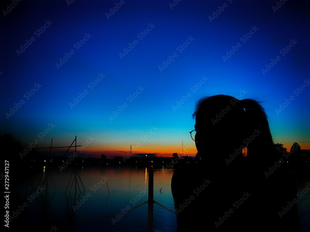 Asian woman is sitting Along the water at dusk, with the sunset  