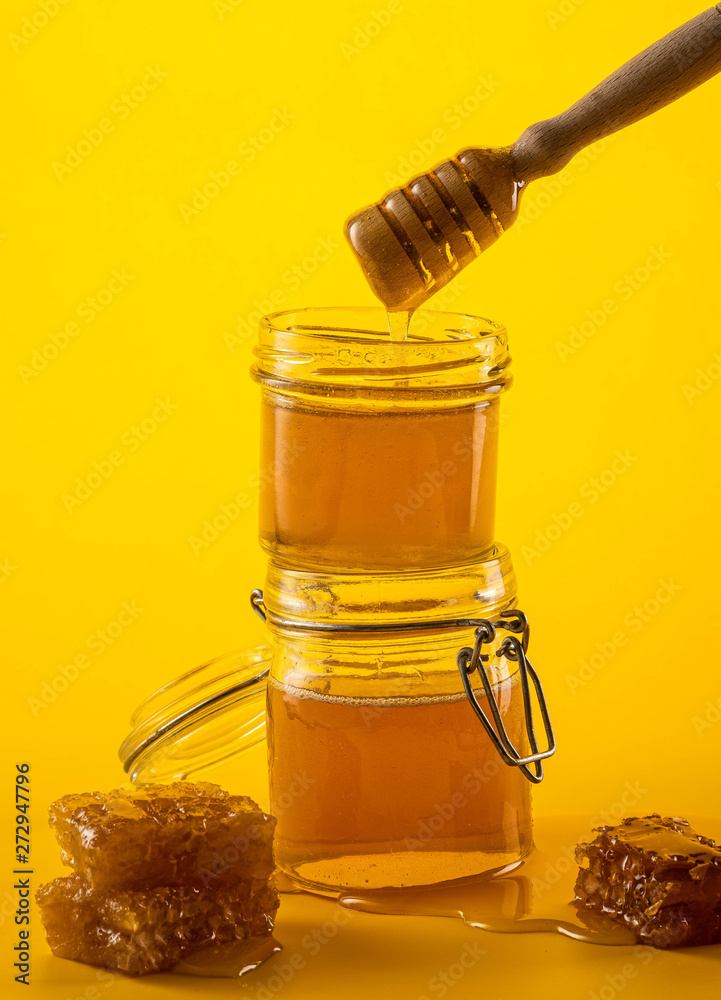 Two jars of honey with honeycombs and a stick on a yellow background Two jars of honey with honeycombs and a stick on a yellow background